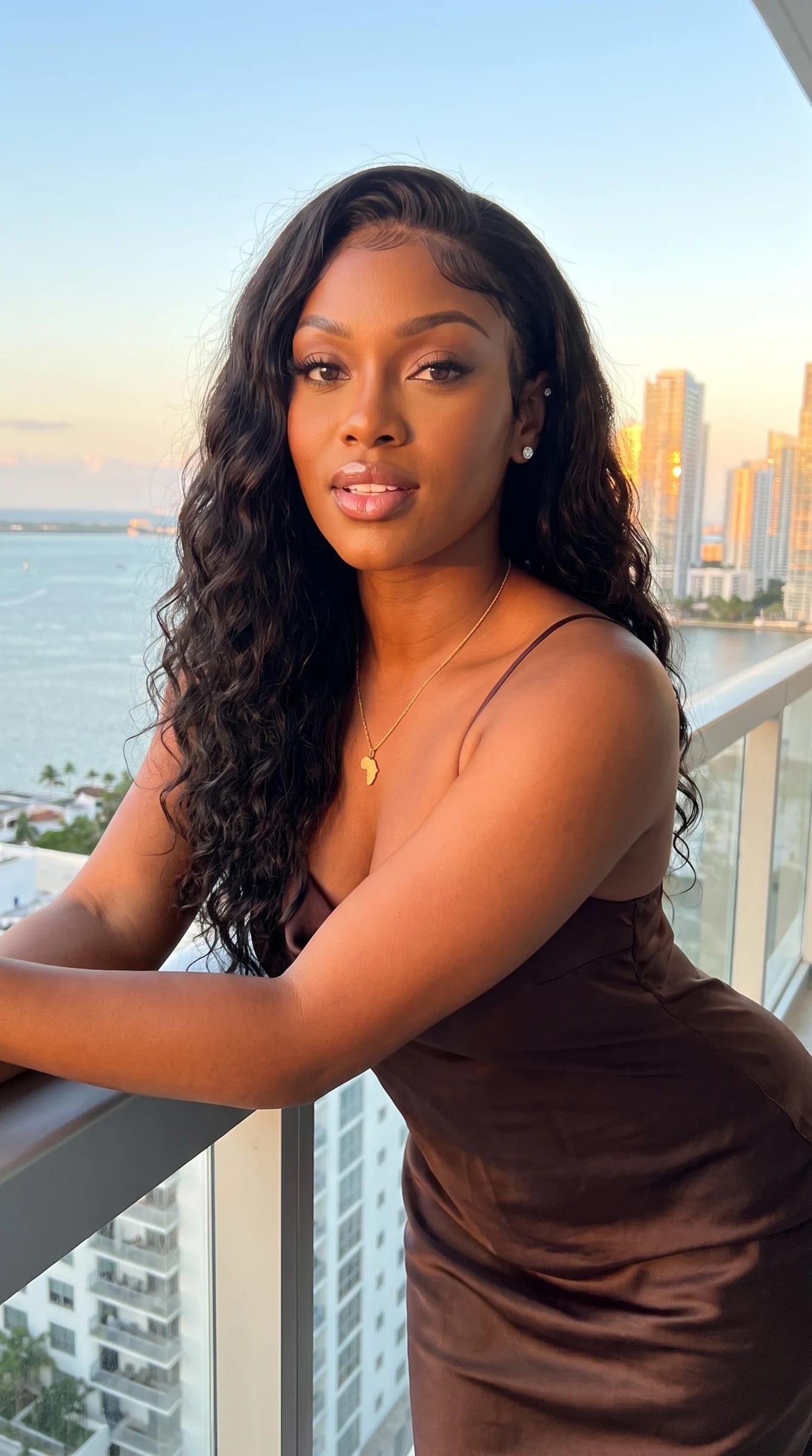 Imani leaning on a Brickell balcony rail at sunset in an espresso silk slip dress